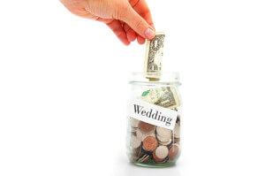 hand putting a dollar into a Wedding coin jar -- wedding cost concept